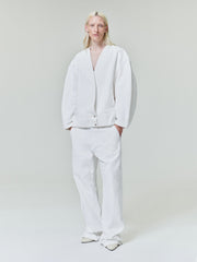 Person with long light blonde hair wearing oversized white jacket and matching loose white pants on light gray background