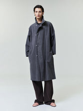 Model wearing a loose dark gray buttoned long coat with high collar and wide sleeves over black pants and pink shoes