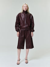 Model wearing a dark brown leather zip-up jacket with matching wide-leg knee-length shorts on a plain background