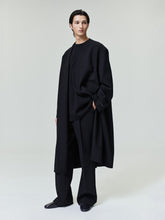 model wearing black double weave wool lapelless coat with double-breasted front and tailored wide-leg pants