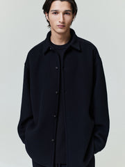 Young man wearing a relaxed black button-up shirt jacket with dropped shoulders and side pockets over a black shirt