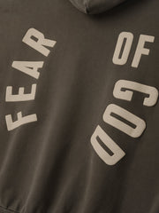 Close-up of faded brown fabric with beige block letters arranged diagonally spelling "FEAR OF GOD" on sweatshirt material