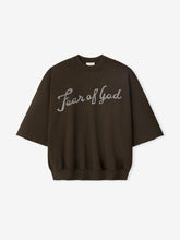 Dark brown sweatshirt with wide-cut sleeves and light gray cursive "Fear of God" text across the chest