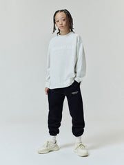 Kids Essentials FW26 Classic Sweatpant worn by a child in black with tapered legs elastic cuffs and subtle logo detail styled with a light gray sweatshirt and sneakers Bottoms