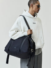 Essentials FW26 Classic Hoodie in cream worn with gray trousers and a black shoulder bag showing a small Fear of God chest logo and relaxed fit Tops