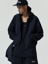Essentials FW26 Classic Zip-Up Hoodie in black worn by a model with raised hood full zip front and kangaroo pockets layered over a tank top Tops