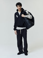 Model wearing White Sox Raglan Half Zip Sport Hoodie in black and gray color blocking with a quarter zip, paired with relaxed black pants and carrying a large black leather bag as casual outerwear.
