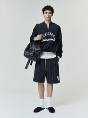 Model wearing White Sox Half Zip Pullover in black with white "Chicago Essentials" script on front, styled with pinstriped shorts, white socks, black slides, and a black leather backpack.