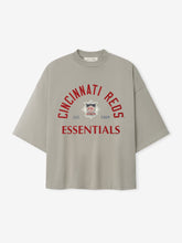 Reds NL Merch Tee in a muted taupe shade featuring relaxed fit with dropped shoulders and bold red "Cincinnati Reds Essentials" text above a vintage-inspired logo on soft fabric.