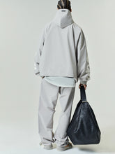 Model wearing a loose light gray Storm Pant paired with a matching oversized hooded jacket, holding a large black textured leather tote bag, viewed from behind.