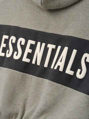 Kids Cropped Relaxed Panelled Hoodie in a muted grey fabric with a contrasting dark panel across the chest featuring raised "ESSENTIALS" lettering for a stylish kids outerwear piece.