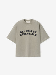 Kids Merch Tee in soft muted gray fabric featuring bold black rounded text "ALL VALLEY ESSENTIALS" in a curved layout for a casual, comfortable kids' top.