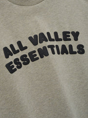 Kids Merch Tee in light heather gray fabric featuring bold black bubble letters spelling "ALL VALLEY ESSENTIALS" in an arched design for a cozy casual kids' top.