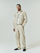 Man wearing an oversized light beige denim jacket over a white graphic tee, paired with loose-fitting Denim 5-Pocket Jeans in a matching light beige tone and black pointed shoes.