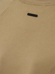 Womens Tri-Blend Shrunken Baseball Tee in a muted dune tone with soft texture, featuring a small black branded patch near the neckline, crafted as a casual top.