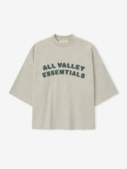 Merch Tee in soft vanilla heather featuring relaxed fit and oversized dark green "ALL VALLEY ESSENTIALS" lettering across the chest for a casual stylish top.
