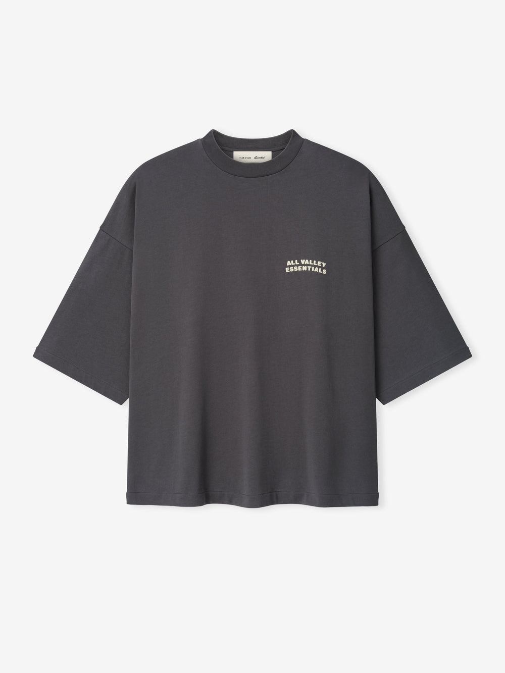 Merch Tee in dark iron grey featuring a relaxed oversized fit with dropped shoulders and small cream text "ALL VALLEY ESSENTIALS" on the chest for a minimalist casual top.