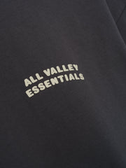 Merch Tee in deep iron grey featuring soft fabric with a minimalist curved cream "ALL VALLEY ESSENTIALS" text printed on the chest for a clean, casual top.