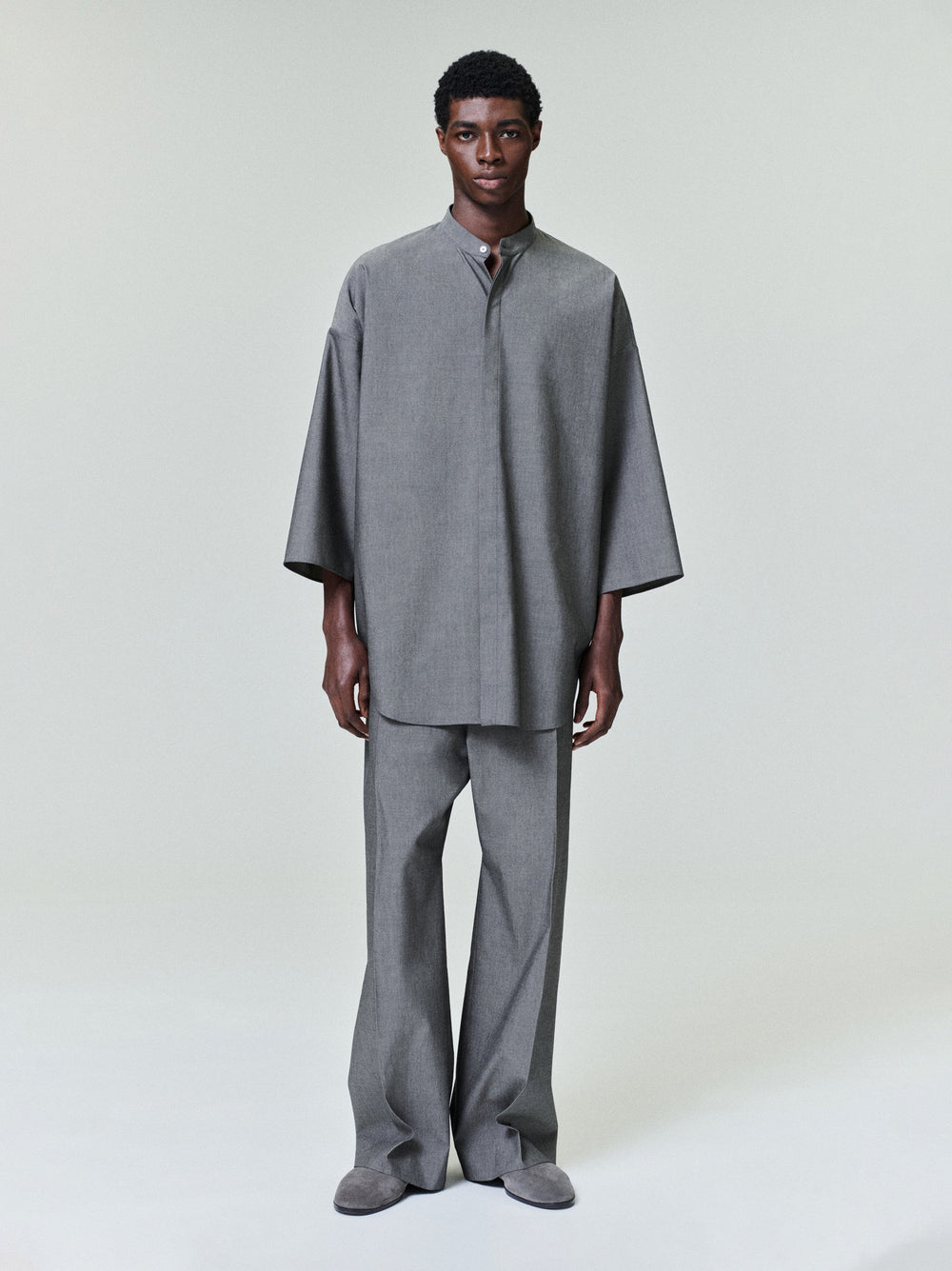 model wearing oversized grey cotton-wool shirt with mandarin collar and wide sleeves paired with matching trousers