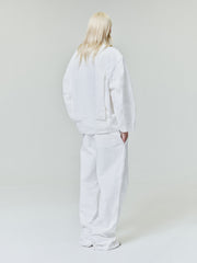 Person with long light blonde hair wearing oversized white jacket and wide white pants standing against plain light background