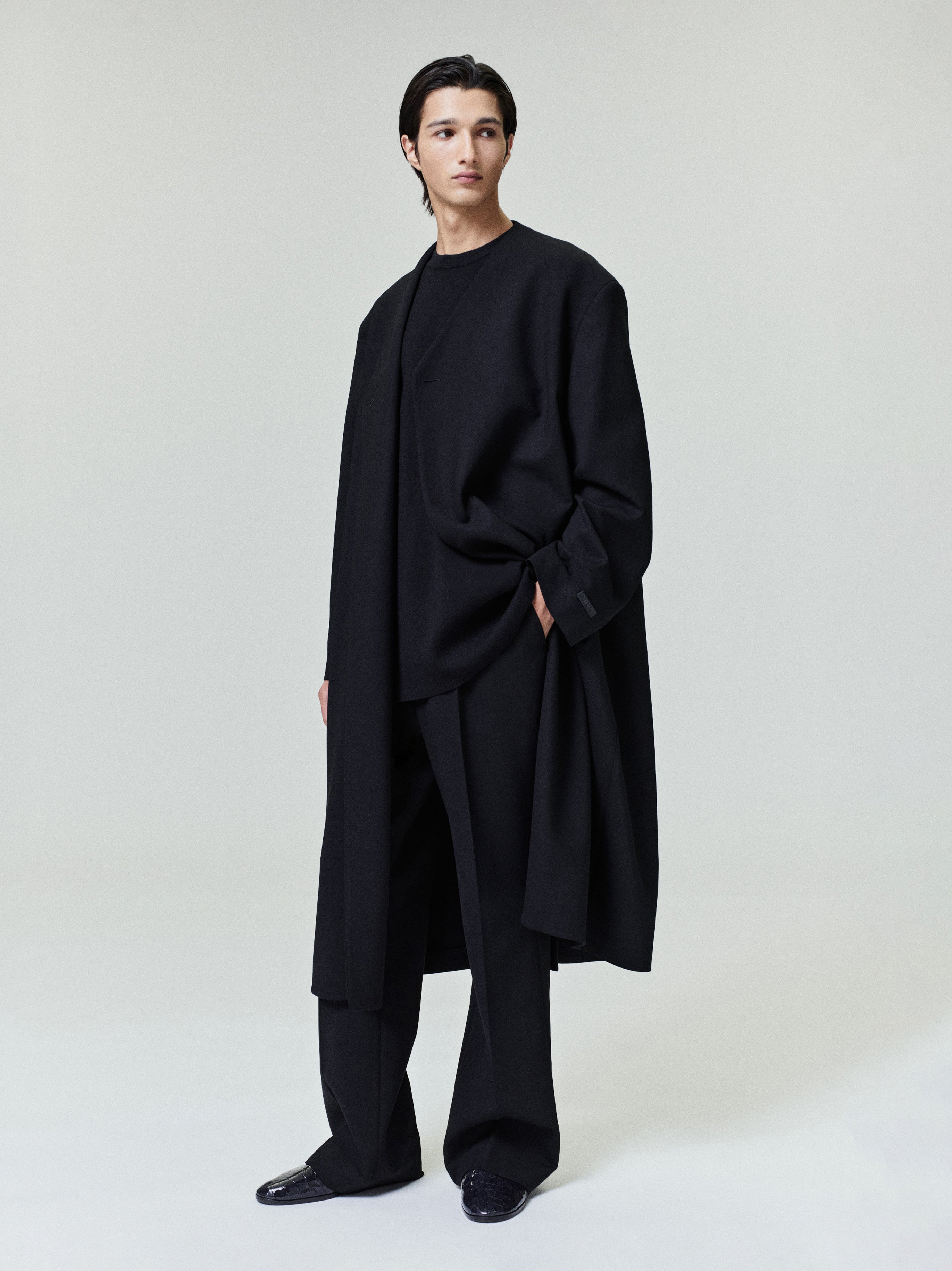 model wearing black double weave wool lapelless coat with double-breasted front and tailored wide-leg pants