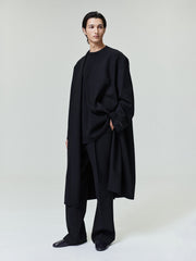 model wearing black double weave wool lapelless coat with double-breasted front and tailored wide-leg pants