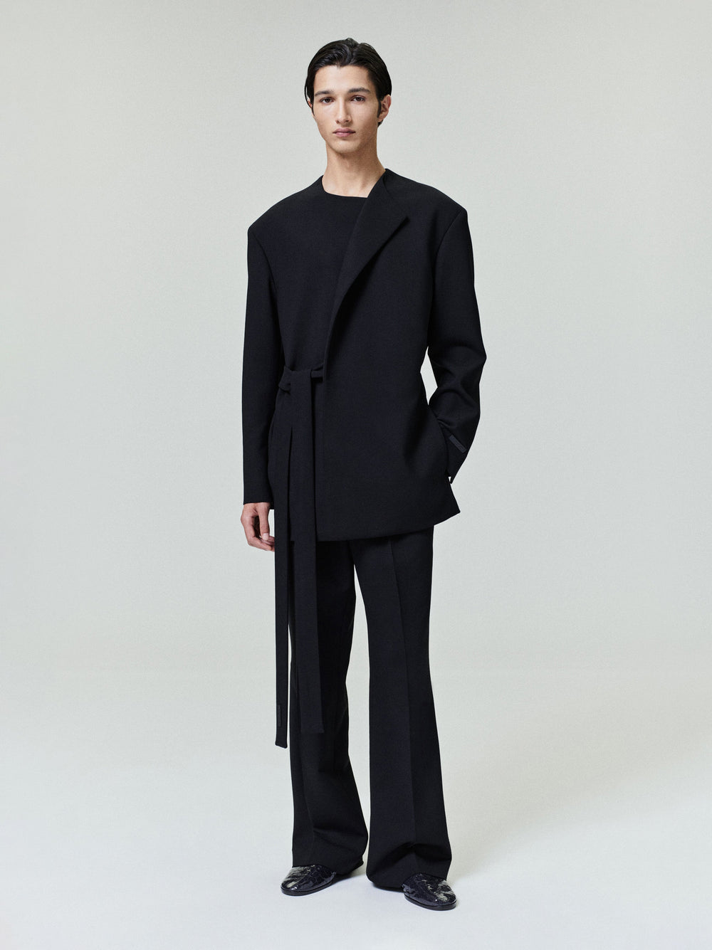 model wearing relaxed tailored black double weave wool crewneck jacket with long belt and matching wide-leg pants