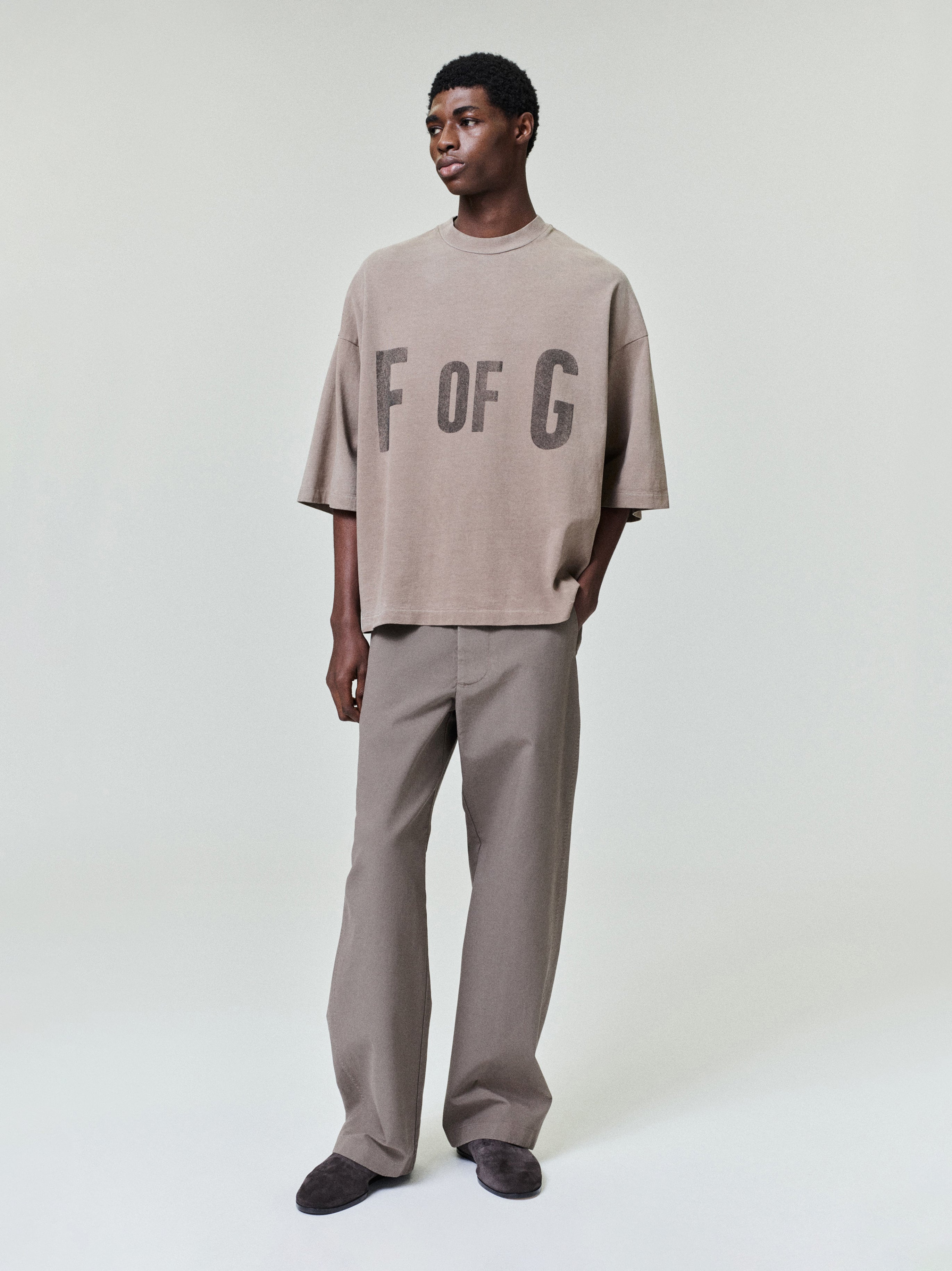 model wearing oversized faded taupe heavyweight cotton tee with large "F OF G" print on front chest