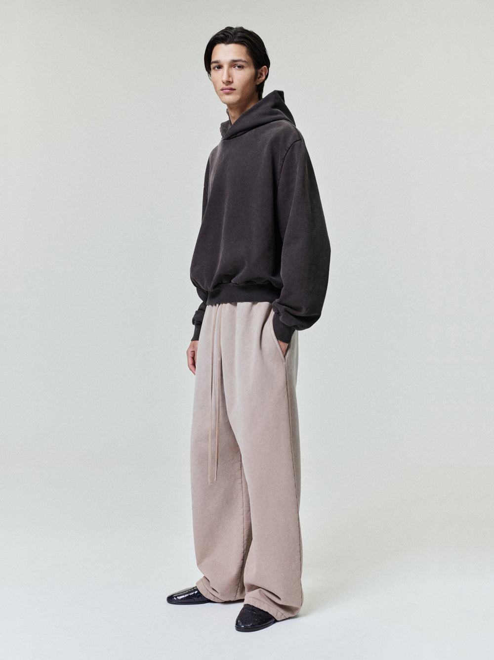 male model wearing light beige wide leg sweatpants with relaxed fit and dark hoodie in minimal studio setting
