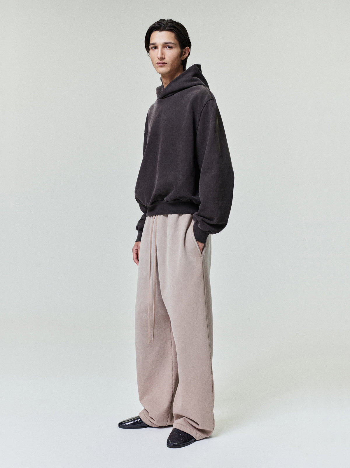 male model wearing light beige wide leg sweatpants with relaxed fit and dark hoodie in minimal studio setting