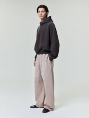 male model wearing light beige wide leg sweatpants with relaxed fit and dark hoodie in minimal studio setting