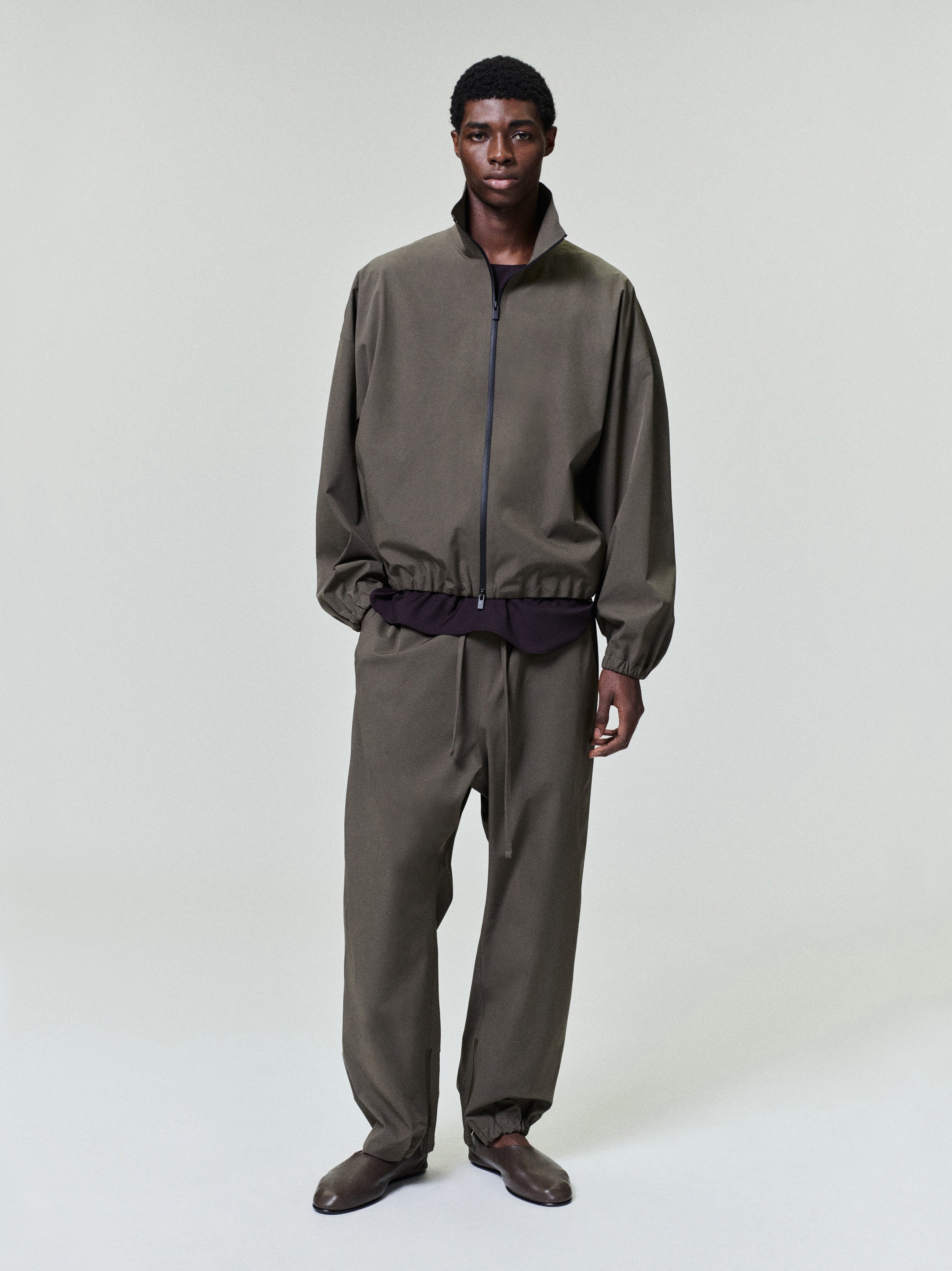 man wearing olive bonded nylon tech track jacket and matching pants with elasticated cuffs and collar