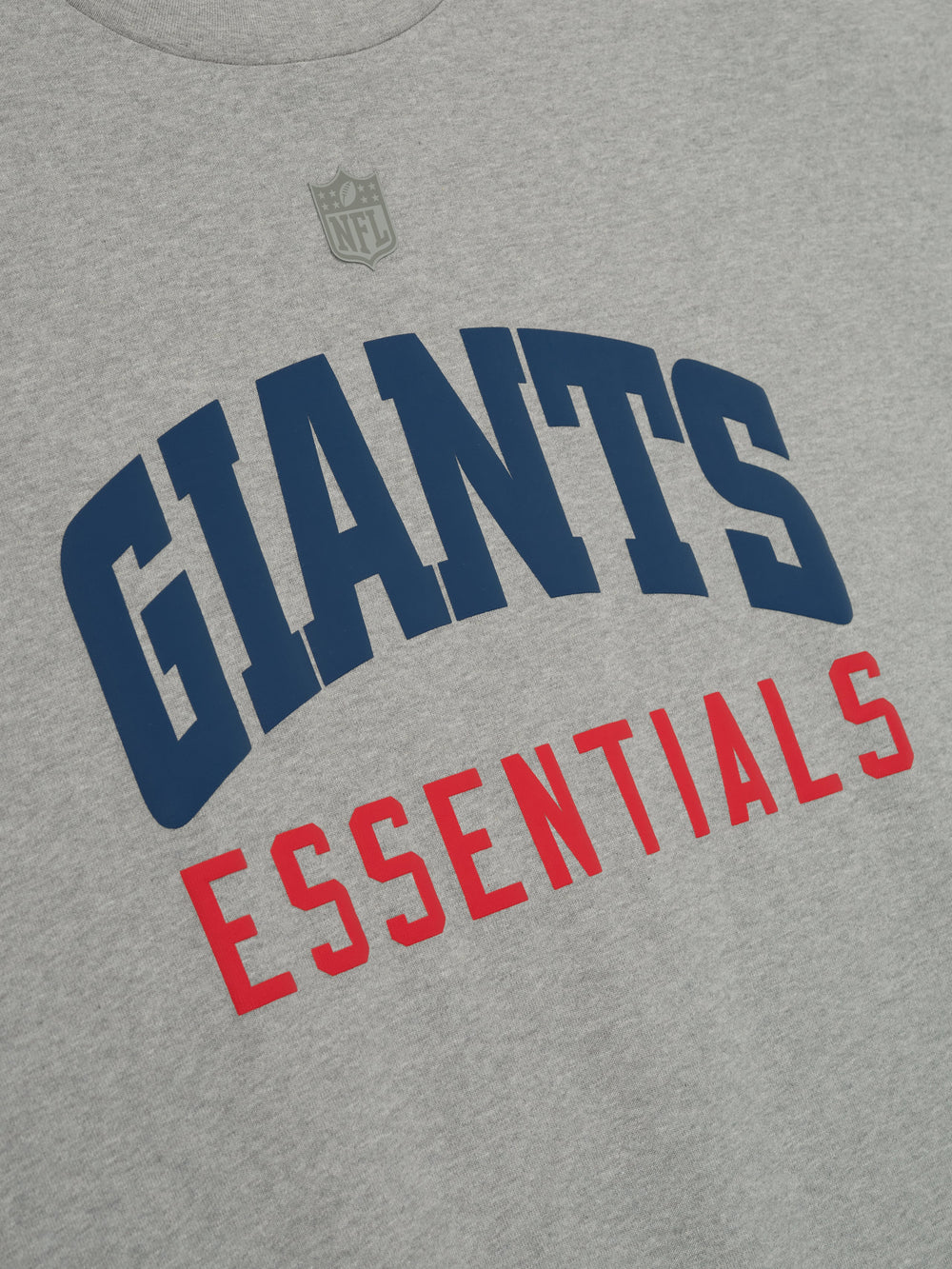 Close-up of concrete heather Giants 90s 3/4 Sleeve Football Tee showing navy Giants and red Essentials text on chest