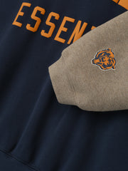 Close-up of Bears Sport Hoodie showing orange Essentials text on dark sapphire fabric and gray sleeve with small bear logo patch