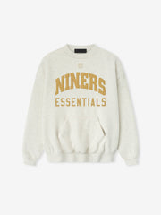 Front view of a light gray Forty Niners Sport Crewneck featuring large gold "NINERS" text arched above smaller "ESSENTIALS" lettering, with ribbed cuffs and a kangaroo pocket.