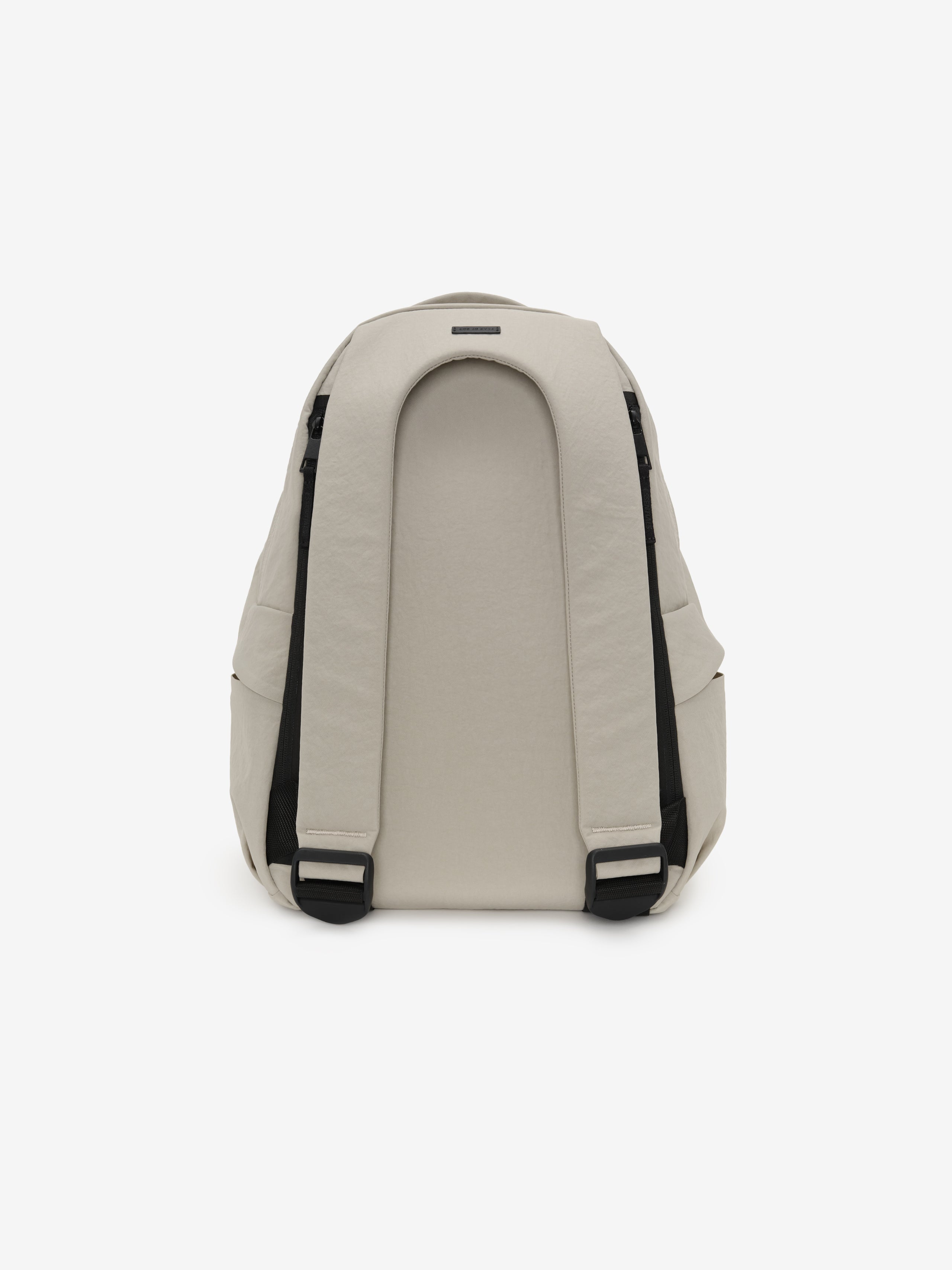 Essentials Backpack in beige shown from the back with padded shoulder straps black adjustment buckles and a curved rear panel against a clean white background