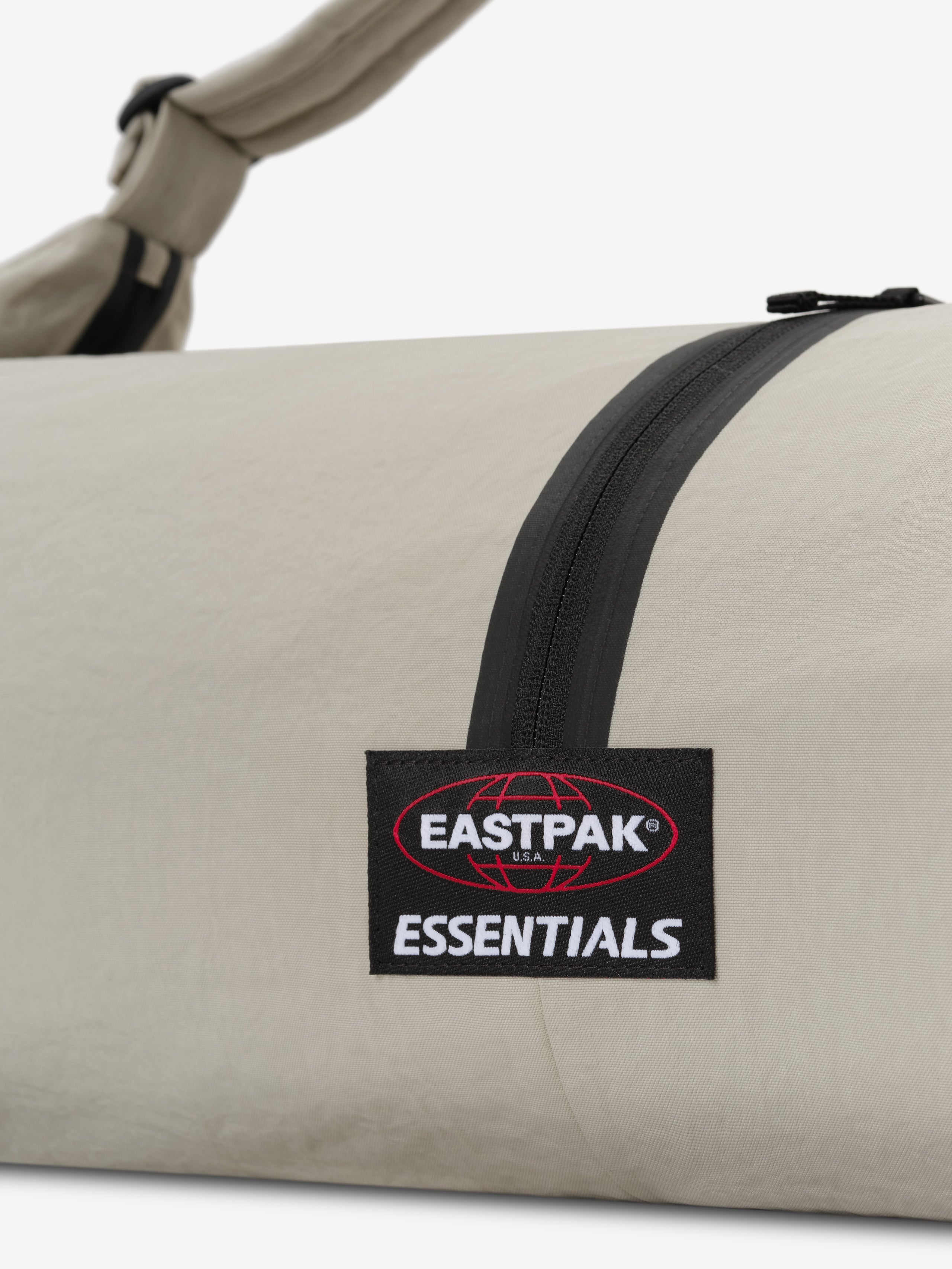 ESSENTIALS SHELL BAG LARGE in light beige with a black curved zipper Eastpak Essentials woven label and shoulder strap shown in close-up