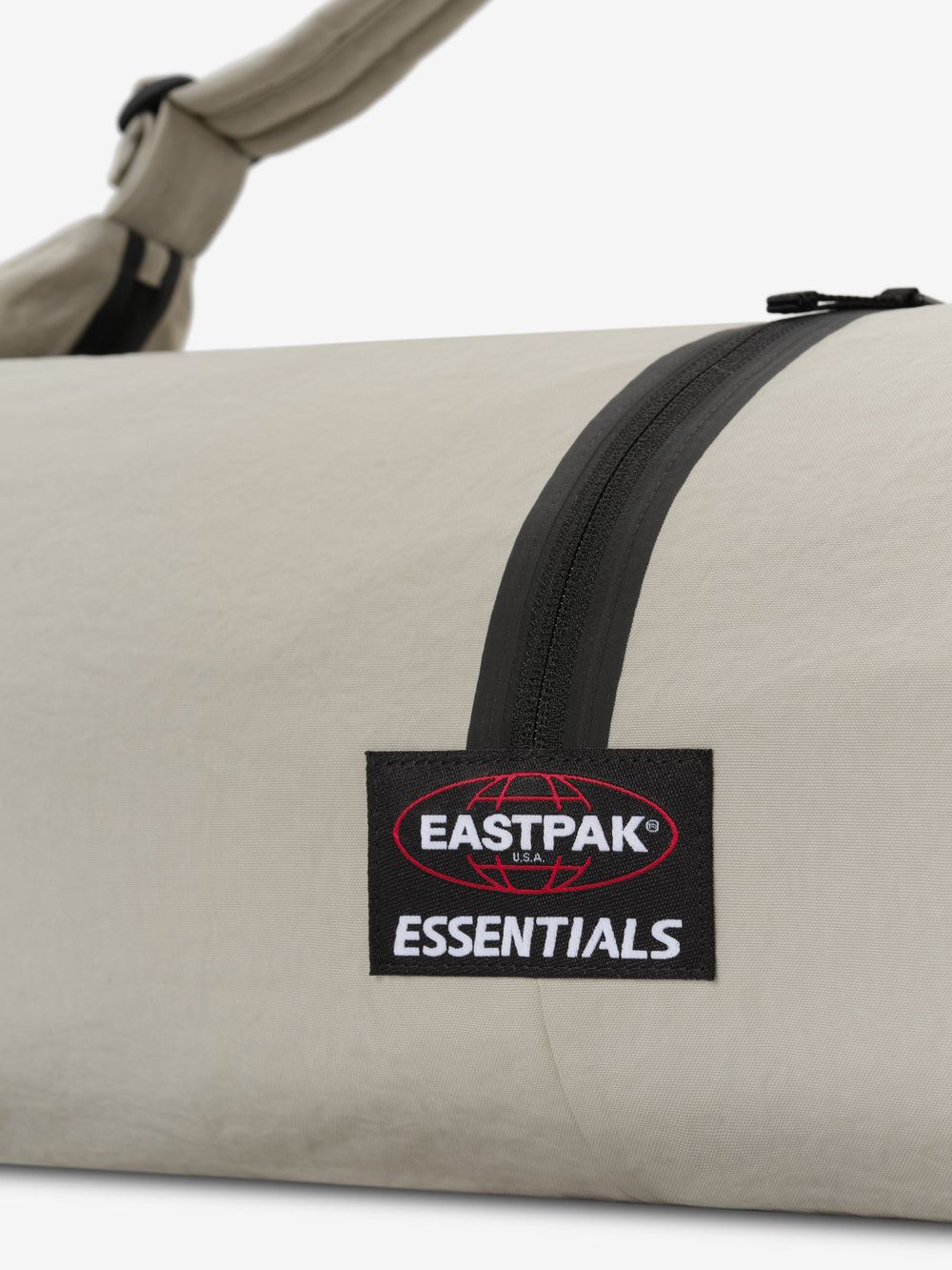 ESSENTIALS SHELL BAG LARGE in light beige with a black curved zipper Eastpak Essentials woven label and shoulder strap shown in close-up