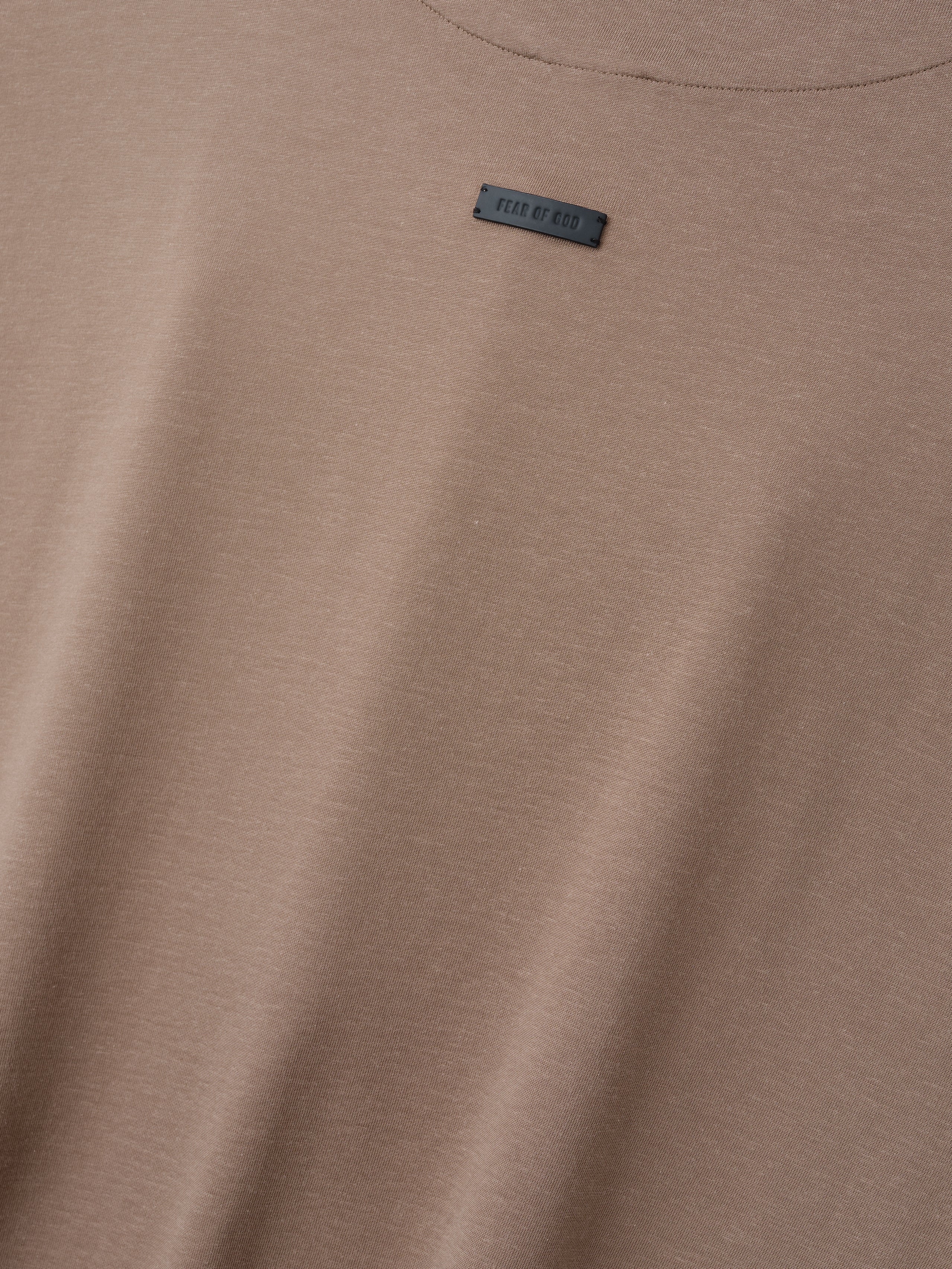 Close-up of a muted light brown t-shirt fabric with a small rectangular black label near the neckline