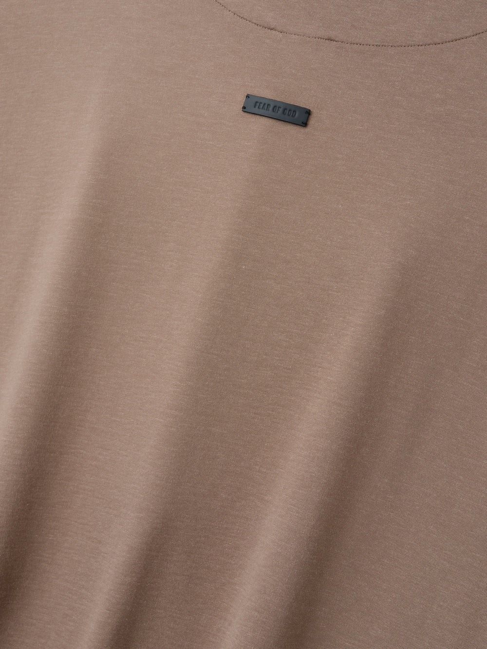 Close-up of a muted light brown t-shirt fabric with a small rectangular black label near the neckline