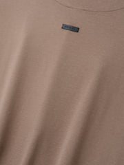 Close-up of a muted light brown t-shirt fabric with a small rectangular black label near the neckline