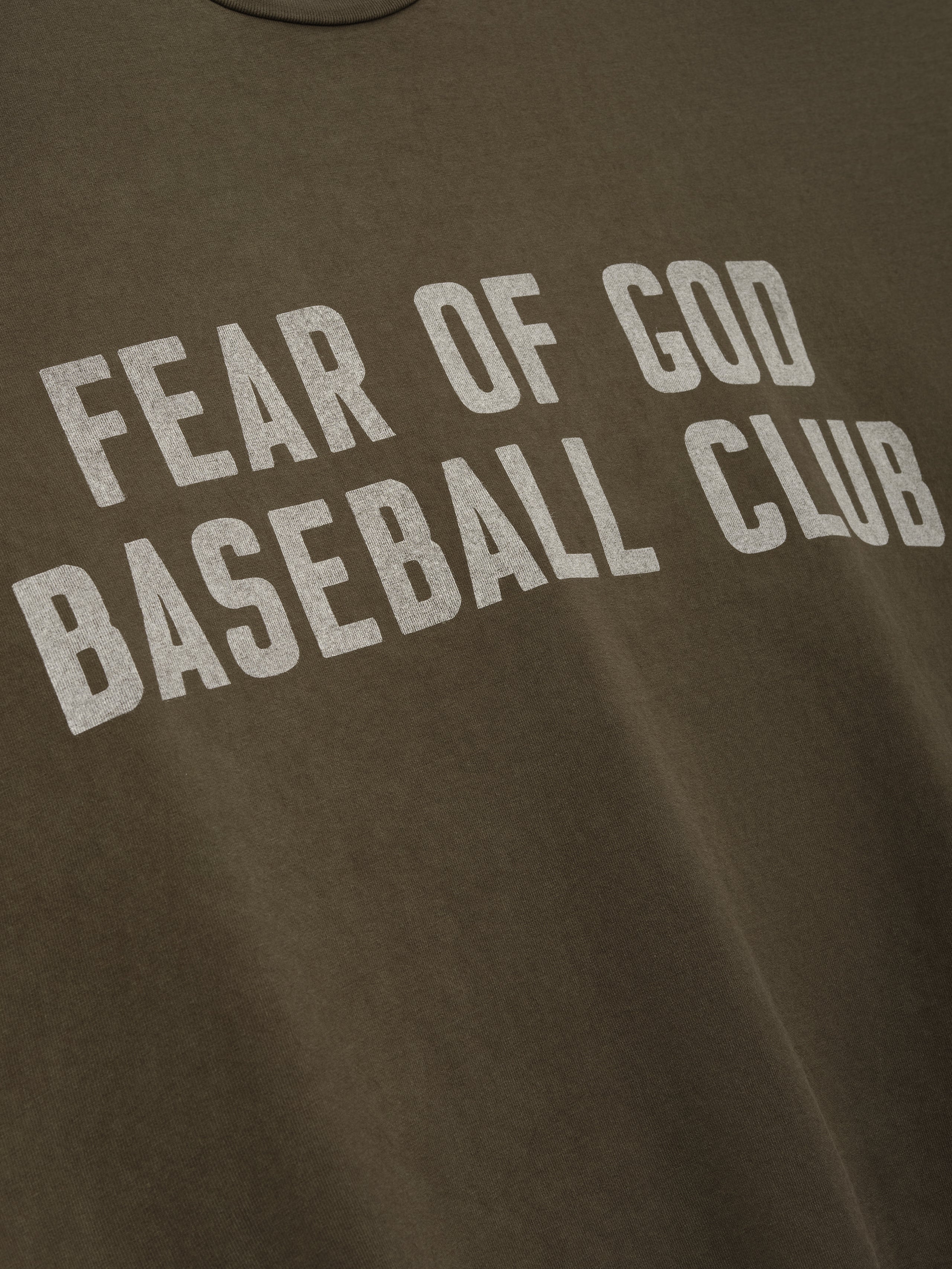 Close-up of faded brown fabric with large distressed white "FEAR OF GOD BASEBALL CLUB" text printed across front
