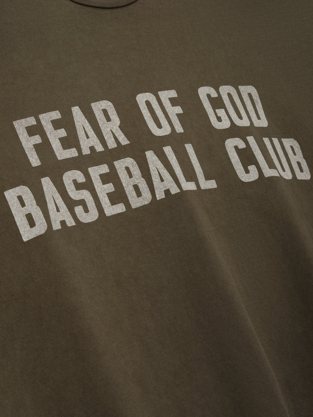 Close-up of faded brown fabric with large distressed white "FEAR OF GOD BASEBALL CLUB" text printed across front
