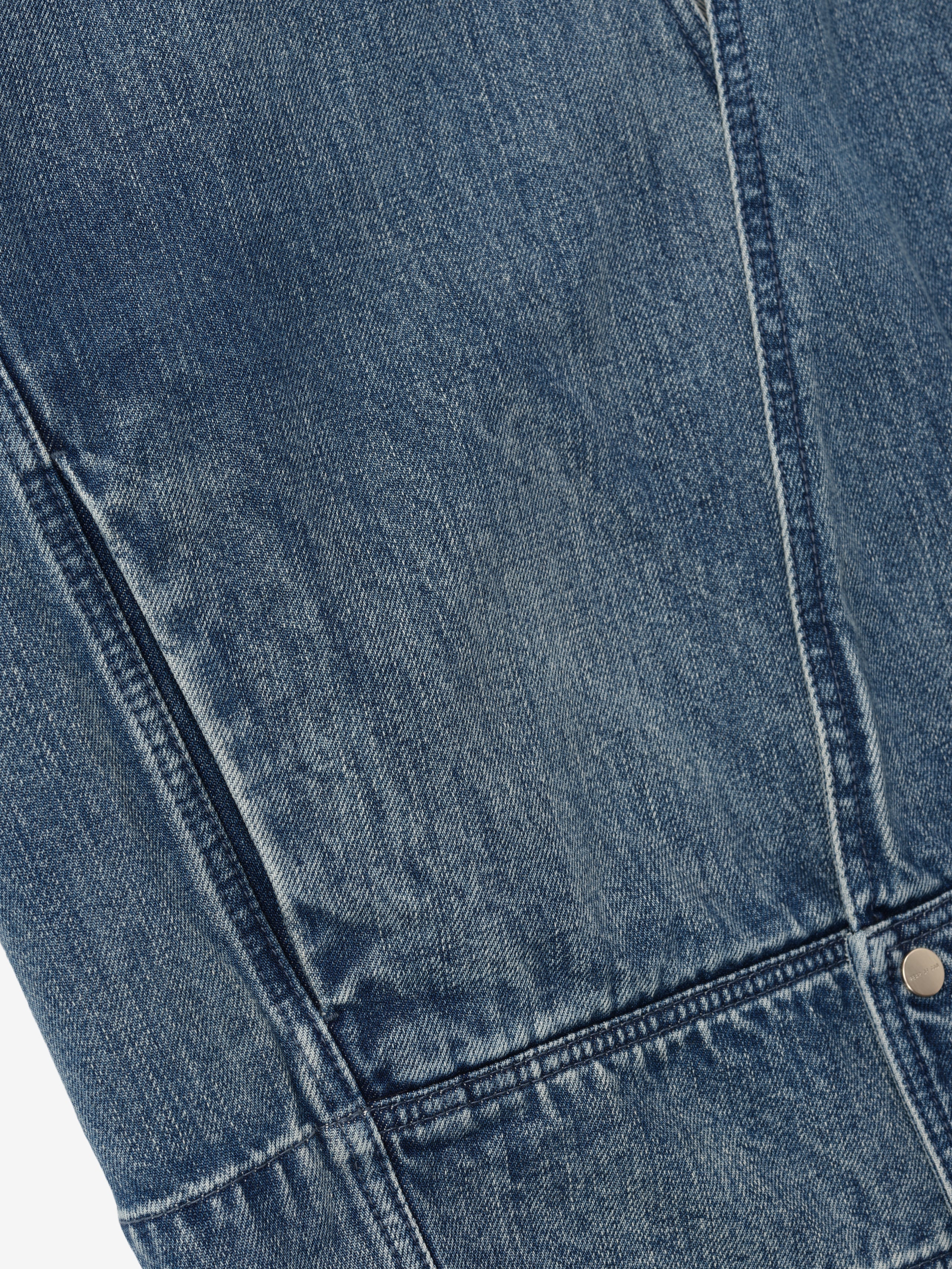 close-up of blue indigo denim fabric with detailed stitching and metal rivet on lapelless jacket panel