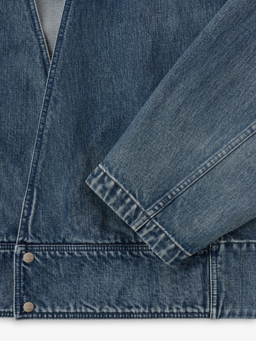 close-up of men's blue indigo denim lapelless jacket with visible metal snap buttons and textured classic wash fabric