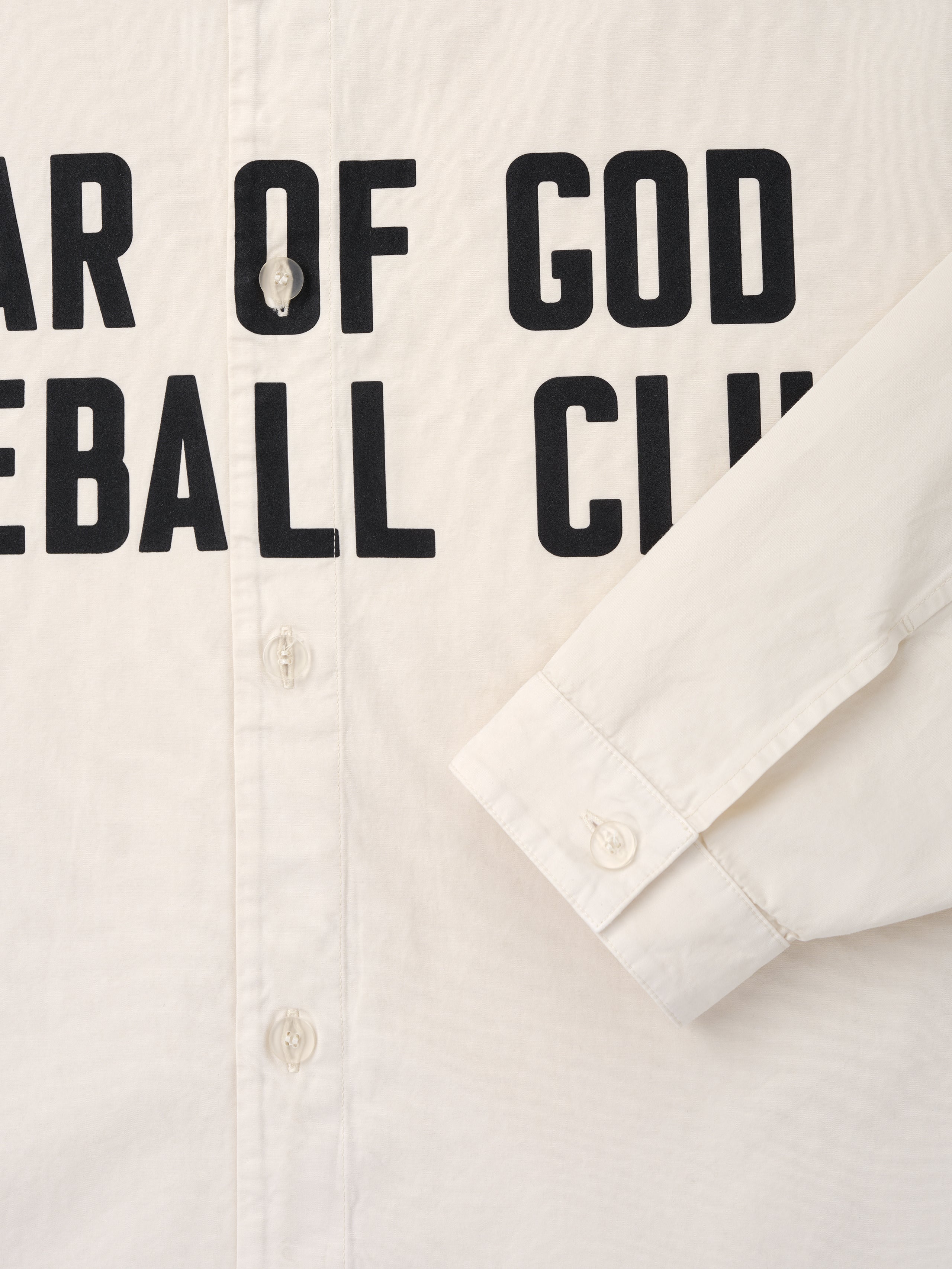 Close-up of natural off-white shirt front with visible buttons and black bold text partially reading "Baseball Club