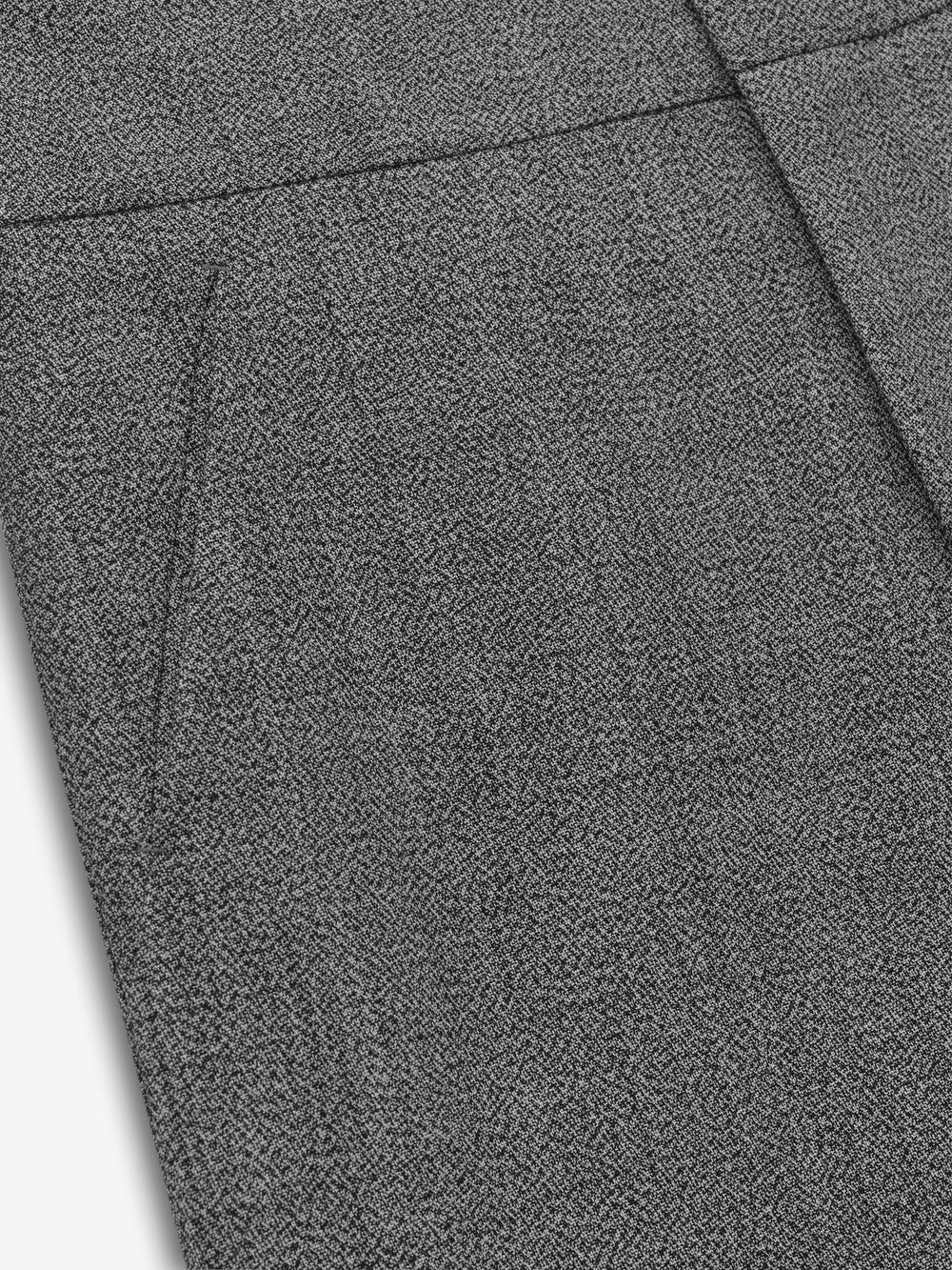 Close-up of off-white fabric with a subtle black herringbone pattern and side seam pocket detail on trousers