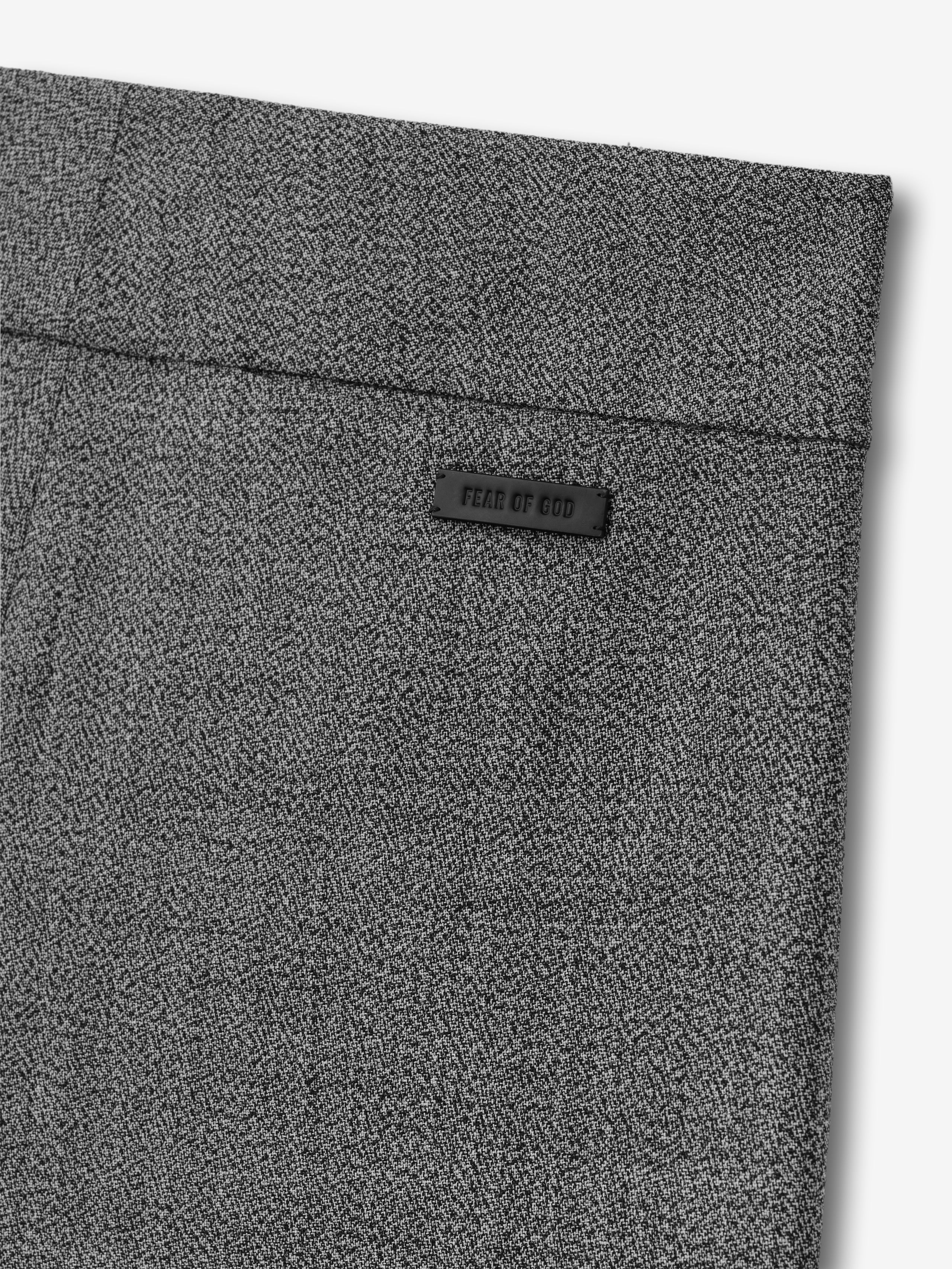 Close-up of gray fabric with a fine herringbone pattern and a small black brand label near the waistband
