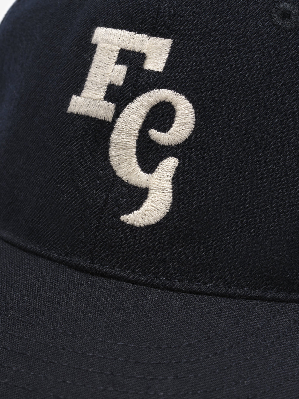 close-up of black textured wool baseball cap with cream felt FG stitched logo on front panel