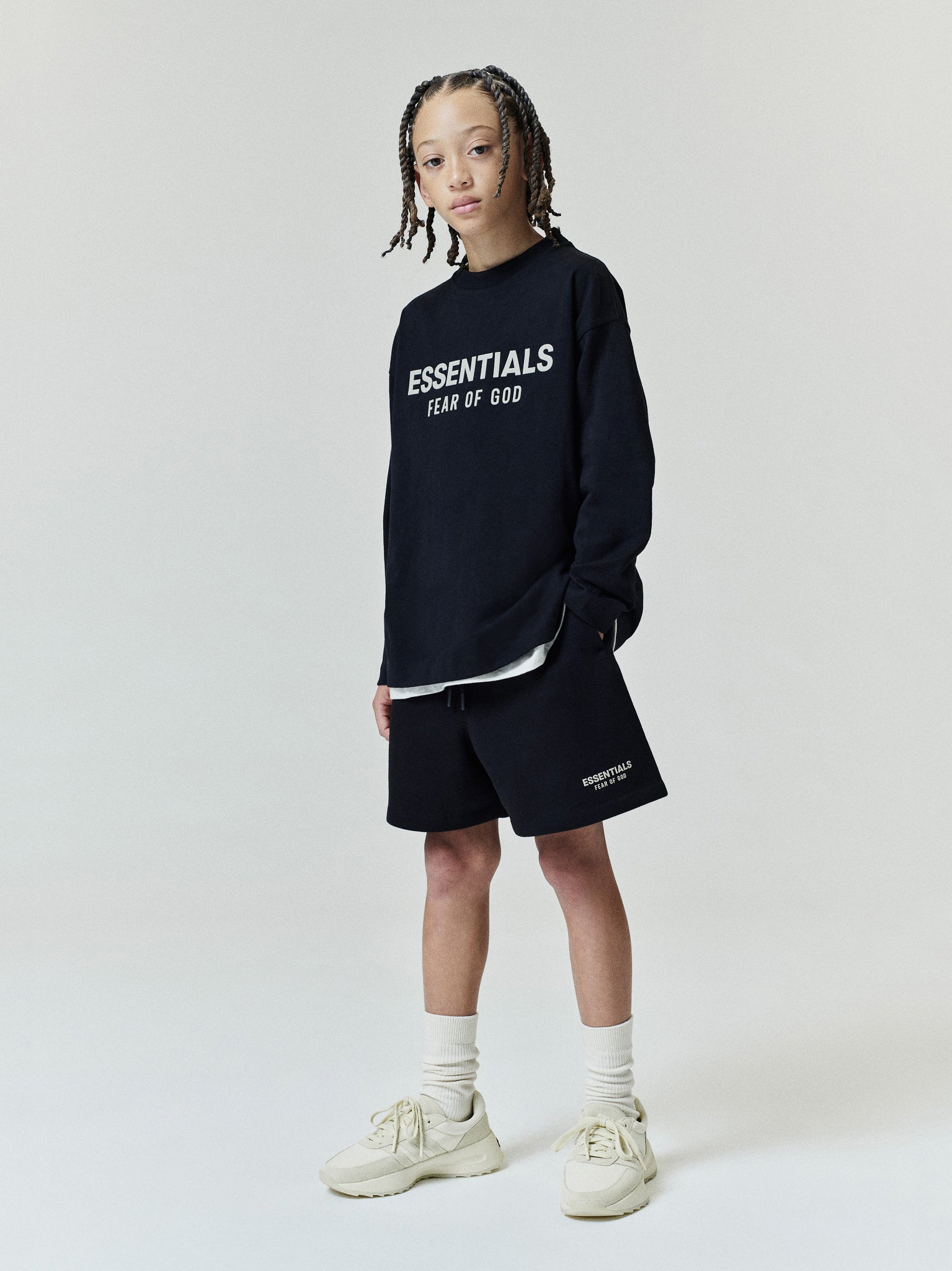 Kids FW26 Classic Sweatshort in black with elastic waistband and relaxed fit styled on a child with an Essentials Fear of God sweatshirt and sneakers Bottoms